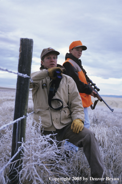 Father and son hunters glassing for big game in a field in winter.