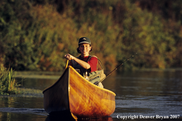 Woman flyfisher in cedar canoe.