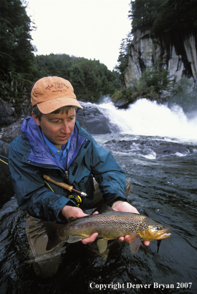 Flyfisherman holding brown trout.  Waterfall in background.