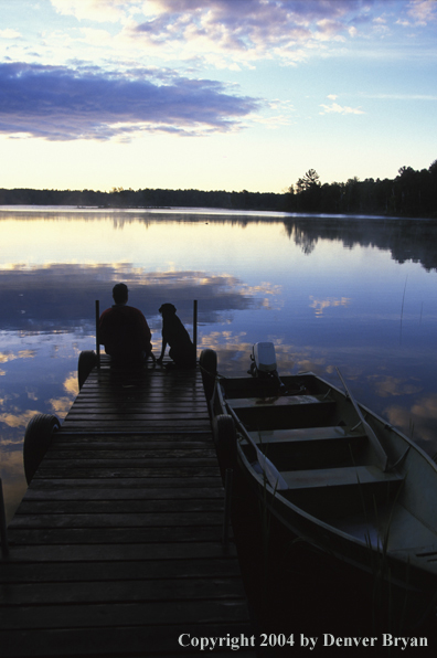 Black Labrador Retriever and owner on dock at sunset