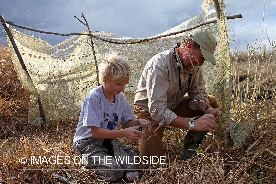 Father and son waterfowl hunters building blind.