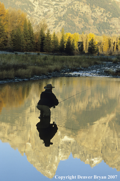 Angler fishing among autumn colors with mountains reflecting in waters