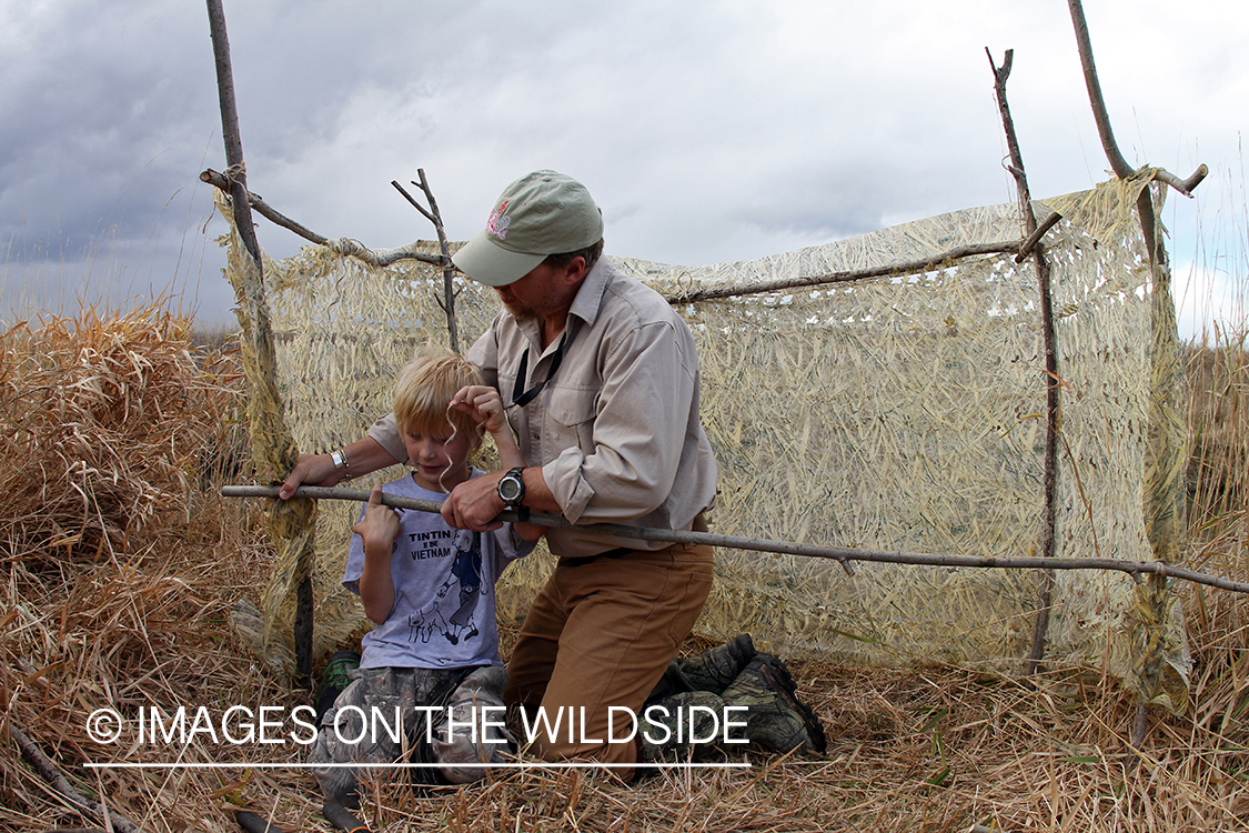 Father and son waterfowl hunters building blind.