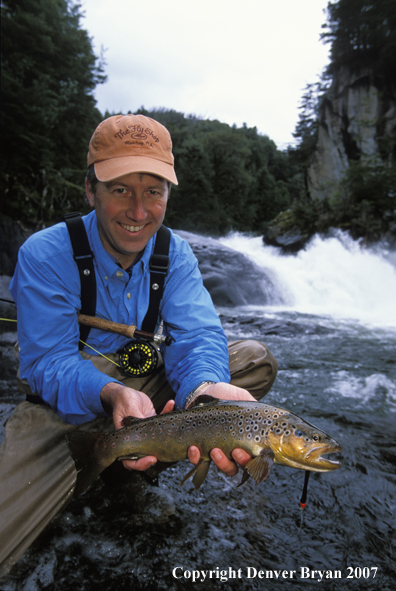 Flyfisherman holding brown trout.  Waterfall in background.