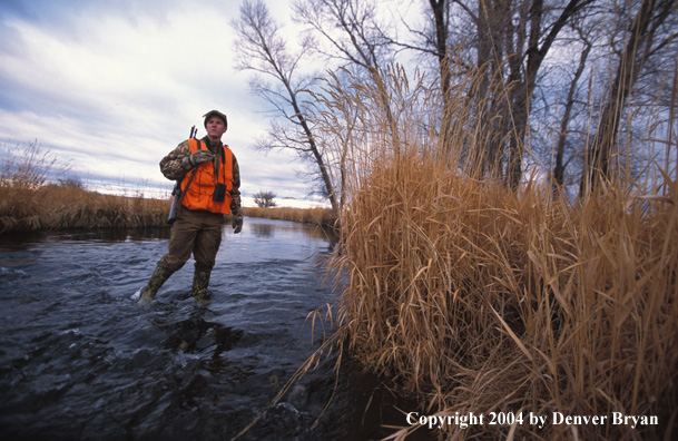 Big game hunter crossing stream.