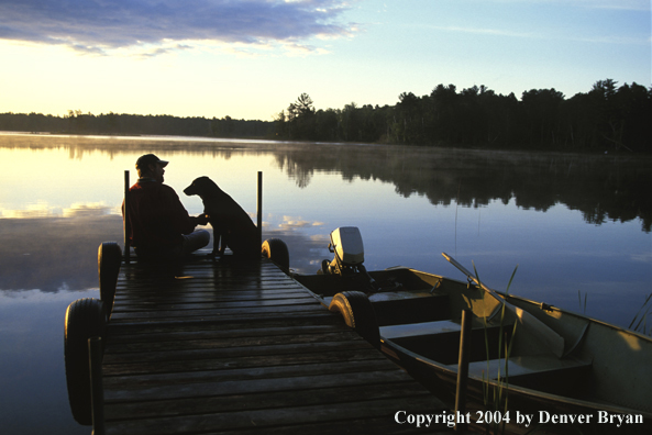 Black Labrador Retriever and owner on dock at sunset