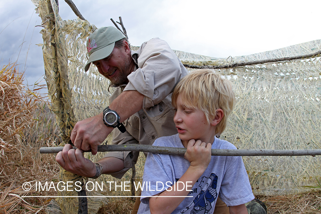 Father and son waterfowl hunters building blind.