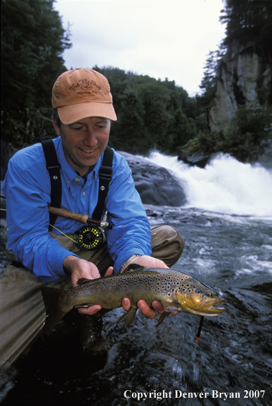 Flyfisherman holding brown trout.  Waterfall in background.