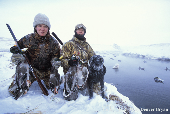 Waterfowl hunters with bagged ducks and black Lab.