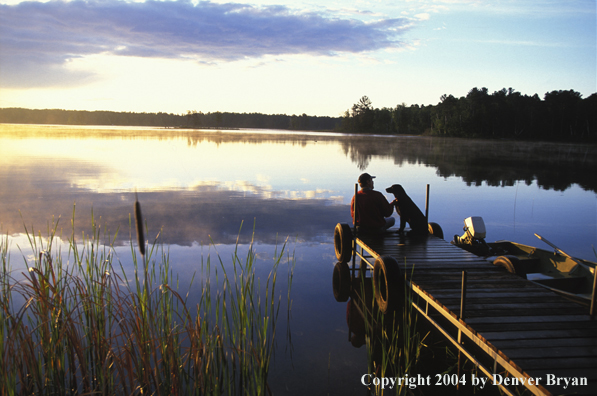 Black Labrador Retriever and fisherman on dock at sunset