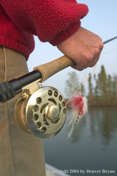 Close up of flyfisherman's hand with fly in hand.  Lake in background