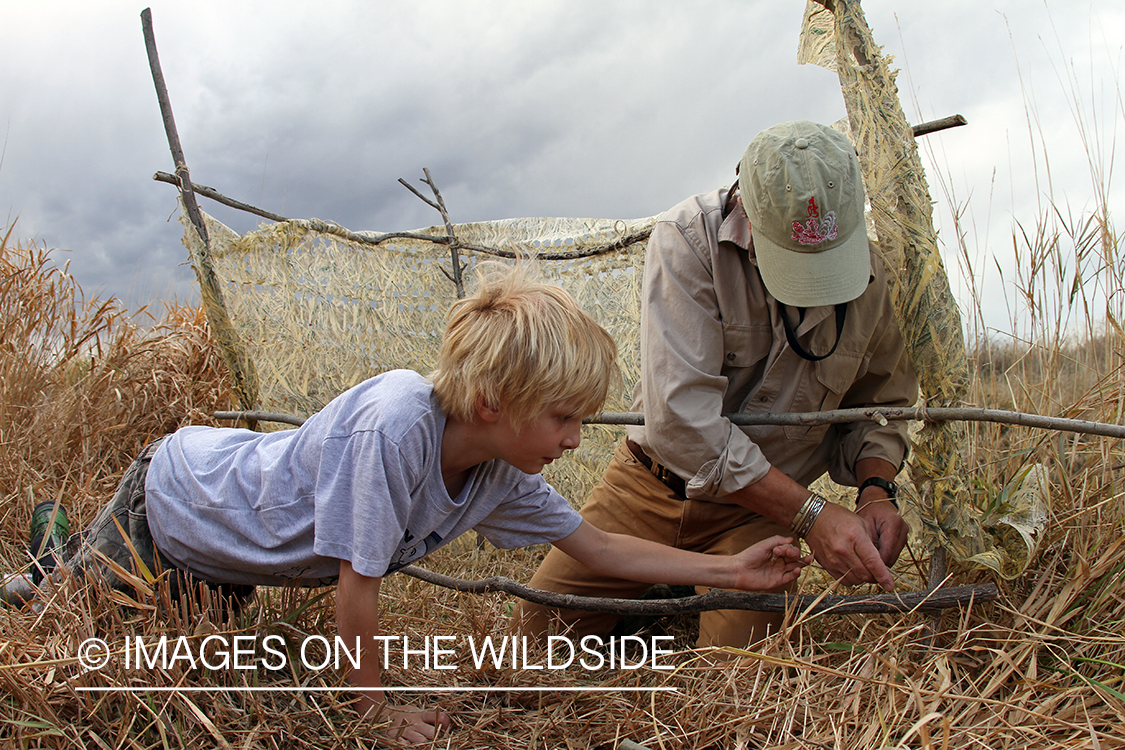 Father and son waterfowl hunters building blind.