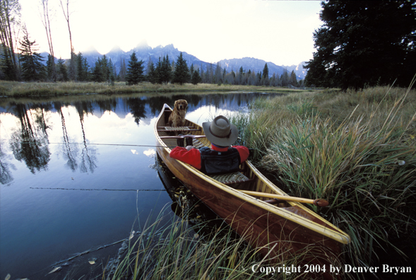 Flyfisherman with Golden Retriever in wooden cedar canoe.  Teton mountains in background.