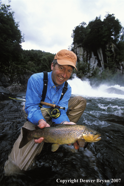 Flyfisherman holding brown trout.  Waterfall in background.