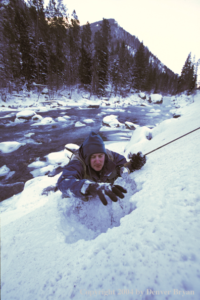 Flyfisherman climbing a snowy bank.