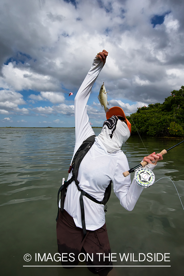 Flyfishing woman pretending to eat small fish on line.