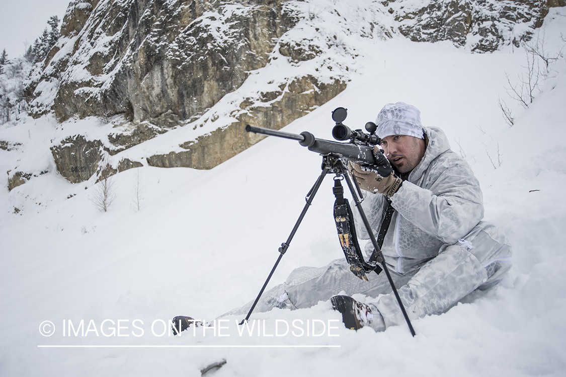 Hunter in snow aiming rifle.