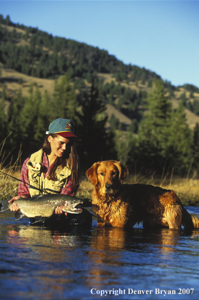 Woman flyfisher with rainbow catch and golden retriever