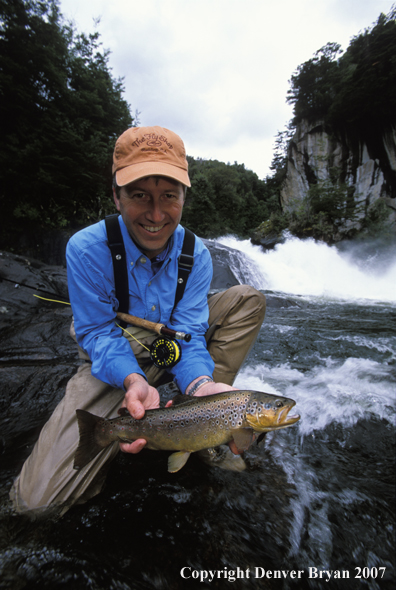 Flyfisherman holding brown trout.  Waterfall in background.