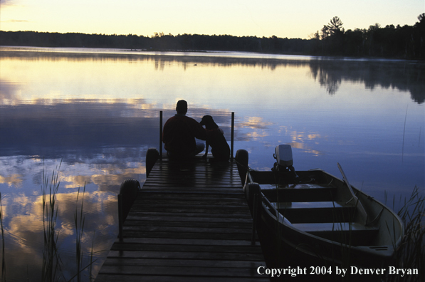 Black Labrador Retriever and fisherman on dock at sunset