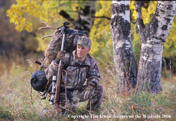 Big game hunter in field packing out caped mule buck.