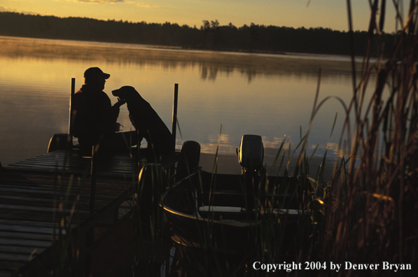 Black Labrador Retriever and owner on dock at sunset