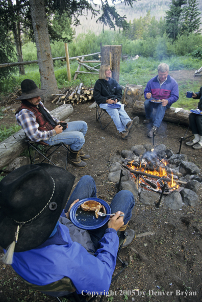 Campers and cowboys sitting around campfire.