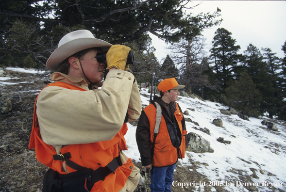 Father and son hunters glassing for big game hunting in a field in winter.