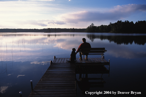 Black Labrador Retriever and owner on dock at sunset