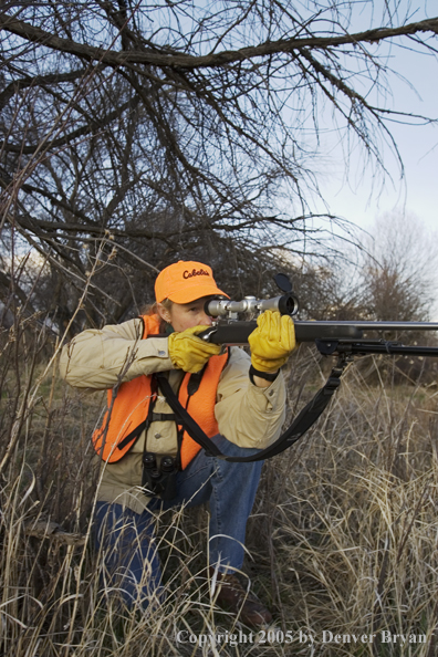 Woman big game hunter aiming/firing for game.