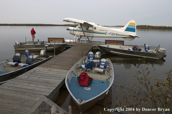 Fisherman fishing on the dock with float plane and fishing boats tied up nearby.  Saskatchewan.