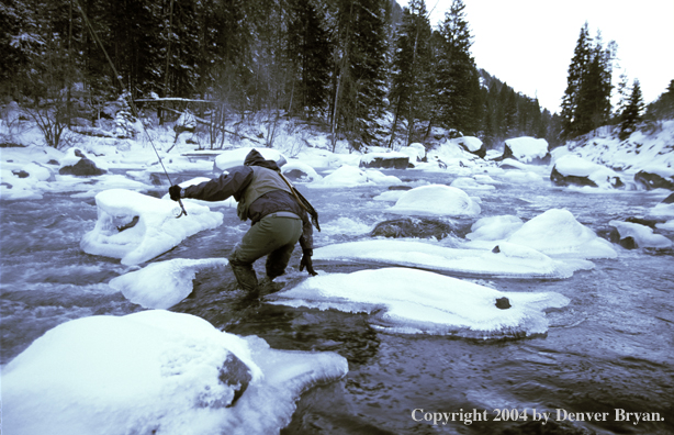 Flyfisherman wading in icy stream.