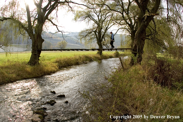 Flyfisherman crossing foot bridge over Pennsylvania spring creek.