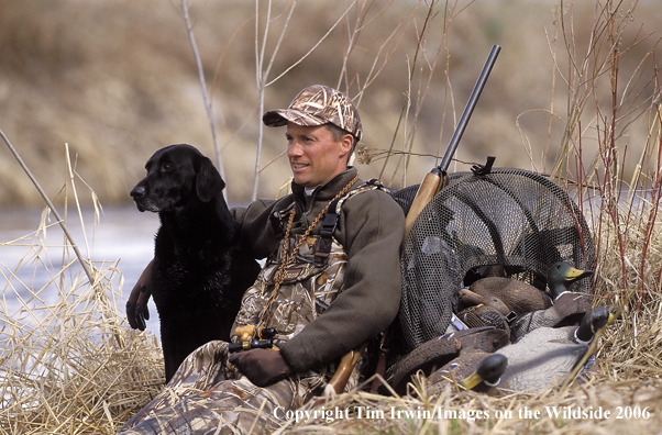 Waterfowl hunter sits in wait with black labrador.