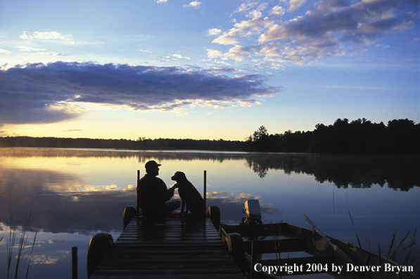 Black Labrador Retriever and fisherman on dock at sunset