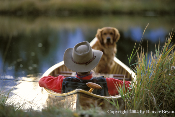 Flyfisherman with Golden Retriever in wooden cedar canoe.  Teton mountains in background.