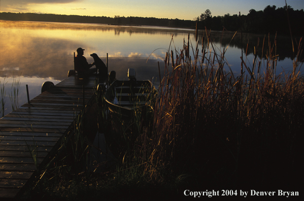 Black Labrador Retriever and owner on dock at sunset