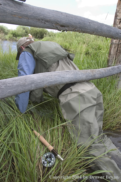 Flyfisherman crawling under fence