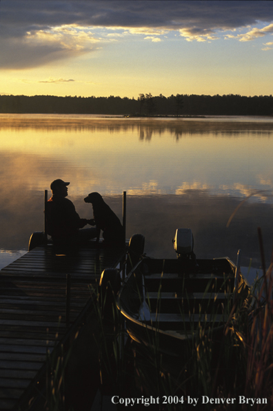 Black Labrador Retriever and fisherman on dock at sunset