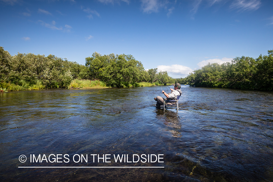 Flyfisherman fishing from camp chair in Sedanka river in Kamchatka Peninsula, Russia.