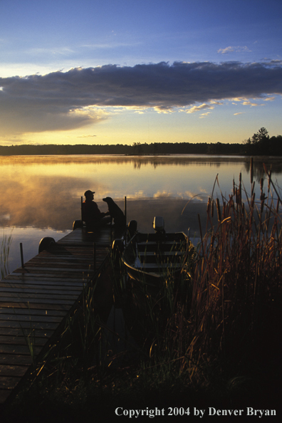 Black Labrador Retriever and owner on dock at sunset