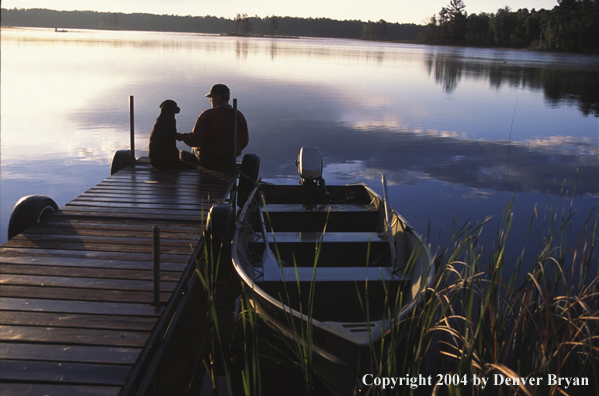 Black Labrador Retriever and fisherman on dock at sunset