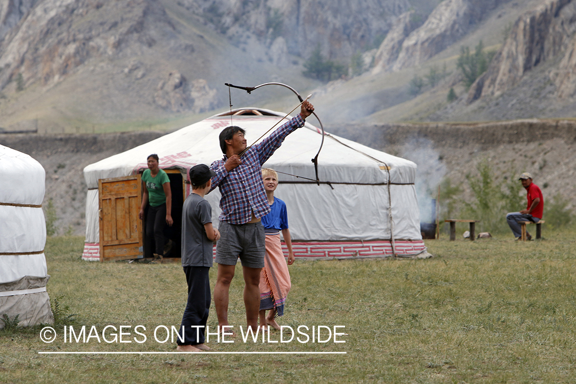 Mongolian man showing boys to shoot native bow.