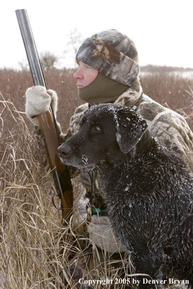 Goose hunter kneeled in field with black labrador at his side. (Close-up)