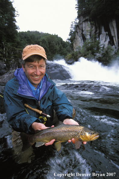 Flyfisherman holding brown trout.  Waterfall in background.