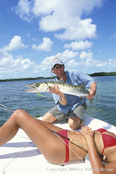 Saltwater flyfisherman with barricuda, woman sunbathing on boat deck.