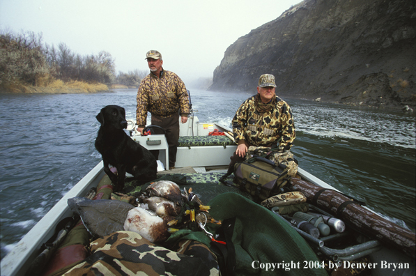 Waterfowl hunters with black Lab and bagged ducks on boat. 