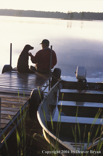 Black Labrador Retriever and owner on dock at sunset