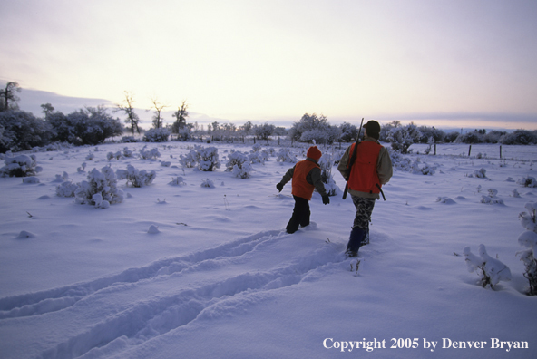 Father and son hunters big game hunting in a snow covered field.