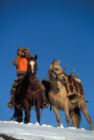 Successful big game hunter glassing from horseback.